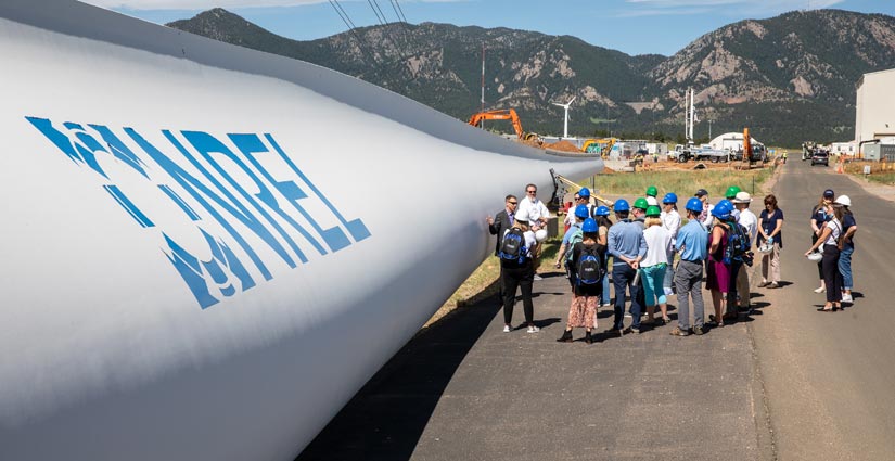 A group of people stand beside a structure, with construction equipment and the mountains in the background.