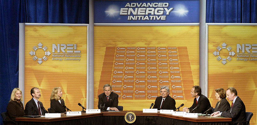 Eight people sitting around a table with microphones and nametags, facing an audience.