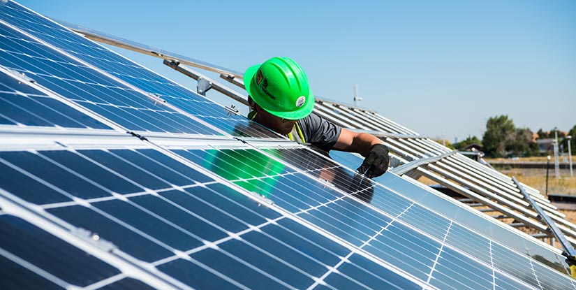 A worker installs photovoltaic panels in a large outdoor solar array.