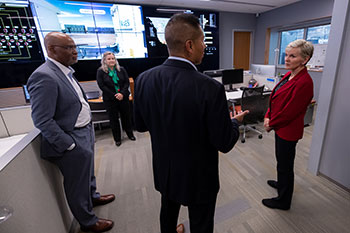 Four people stand in room with large display monitors