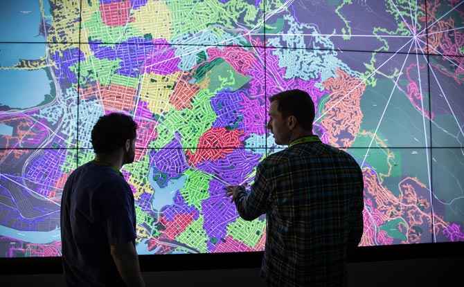 Three NREL researchers talk in front of video screen.