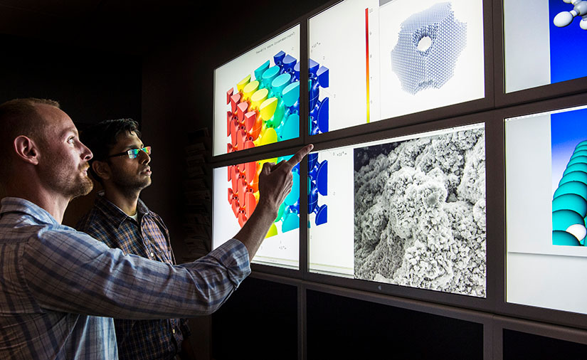 Two researchers facing a wall of computer monitors in a lab.