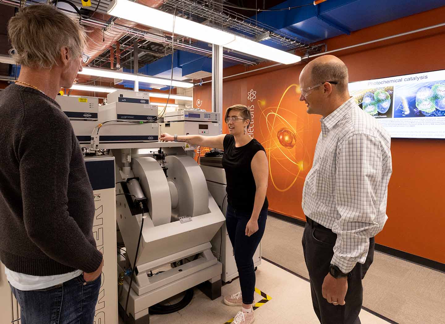 A group of researchers talking and standing next to a machine. 
