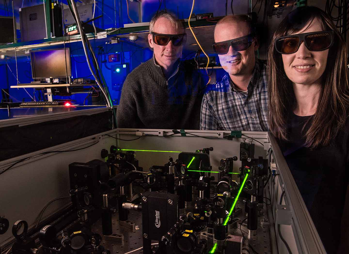 Three people wearing protective tinted glasses in a lab. 