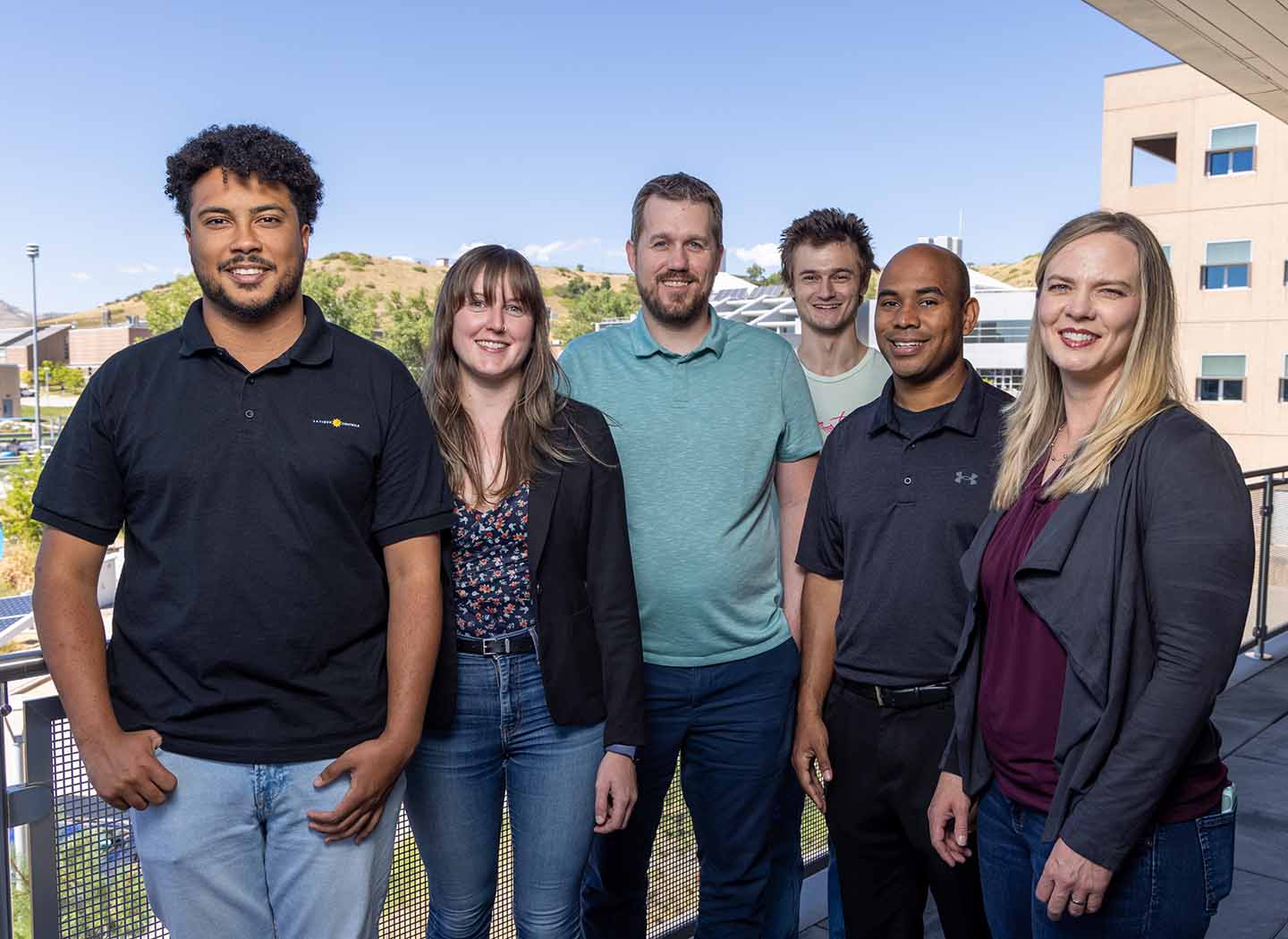 Six people smile for the camera, posed on an outdoor balcony. 