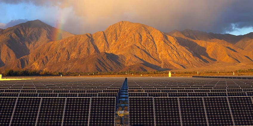 Solar panels in front of a mountains, clouds and a rainbow.