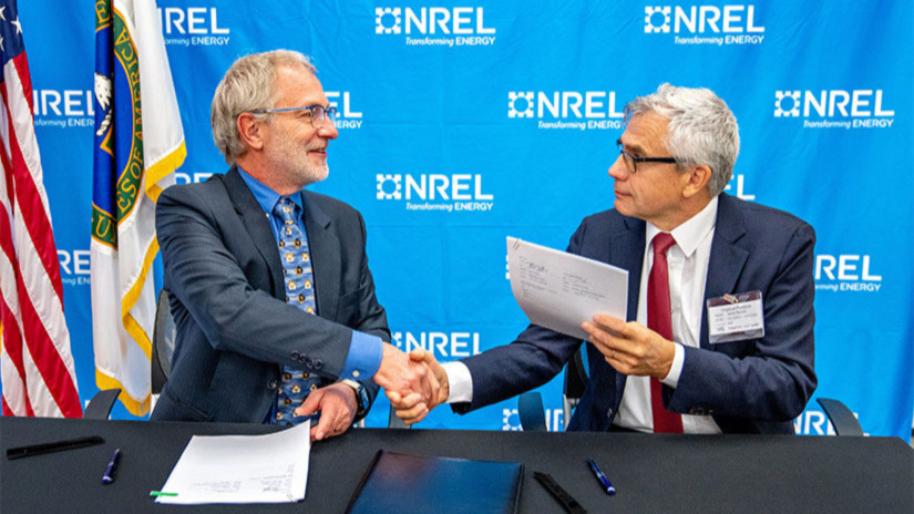 Two people shake hands after signing agreement at table.