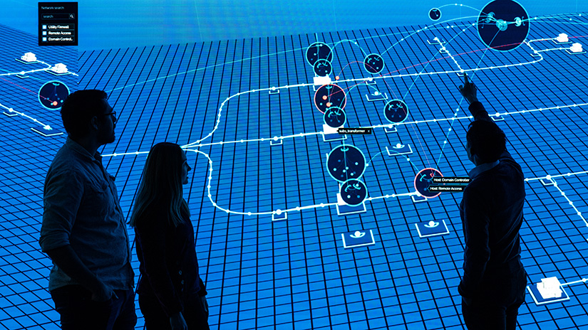 Three people stand in front of large computer display with data on cyber threats