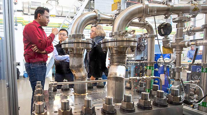 Photo of three researchers talking while looking at a hydrogen electrolyzer.