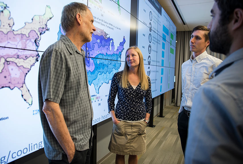 A group of people stand in front of screens with maps and graphics displayed across them.