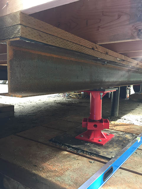 The underside of a home foundation showing a threaded jack supporting a steel beam