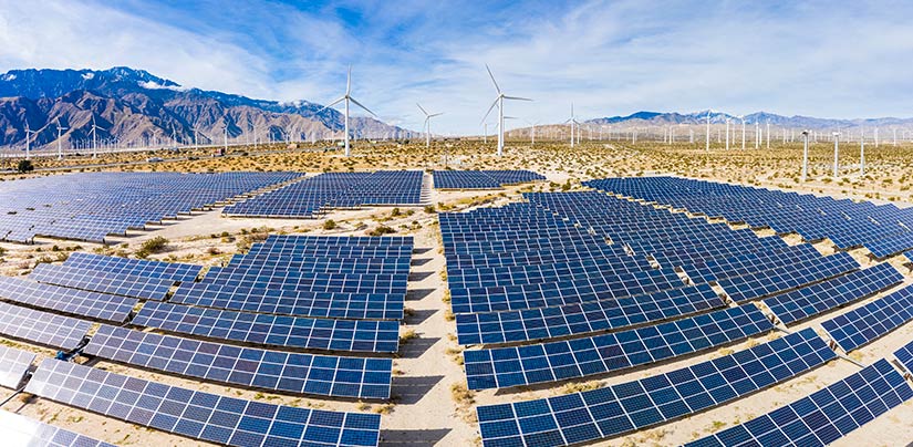 Utility-scale solar photovolatic array with wind turbines in the background.