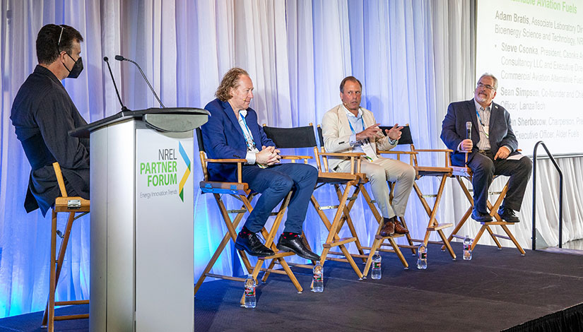 A moderator and four panelists seated on a stage during a panel discussion