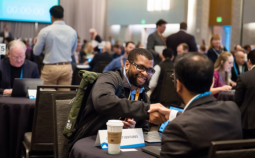 Two men sitting at a table shake hands. 