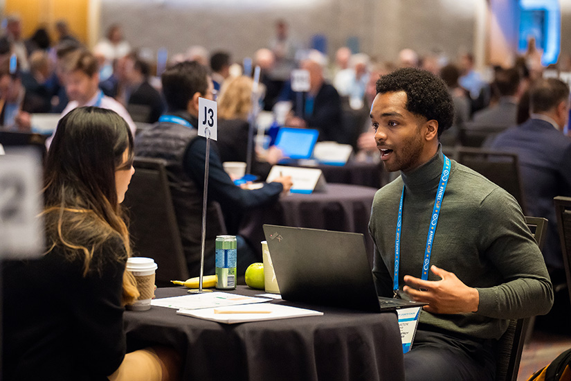 A man and woman sit at a small table talking with other people talking at other small tables around them.