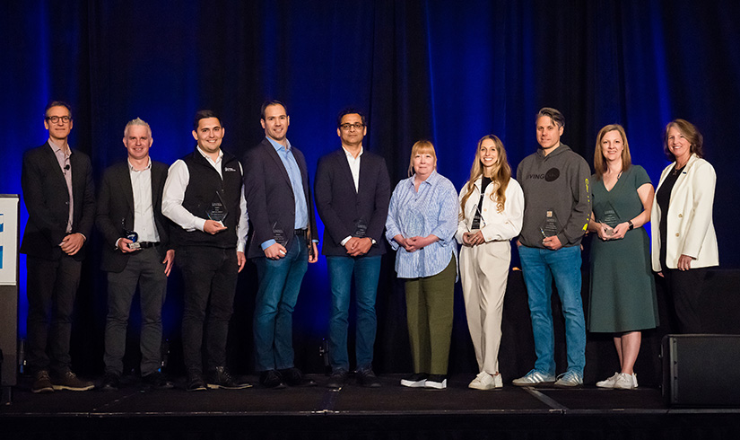 A group of award winners pose on a stage holding their awards.
