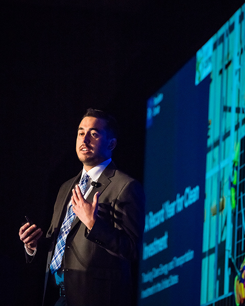 A man stands at a podium with a slide behind him focused on investments in clean technologies.