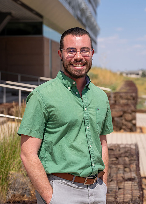 A person with their hands in their pockets stands in front of a building.