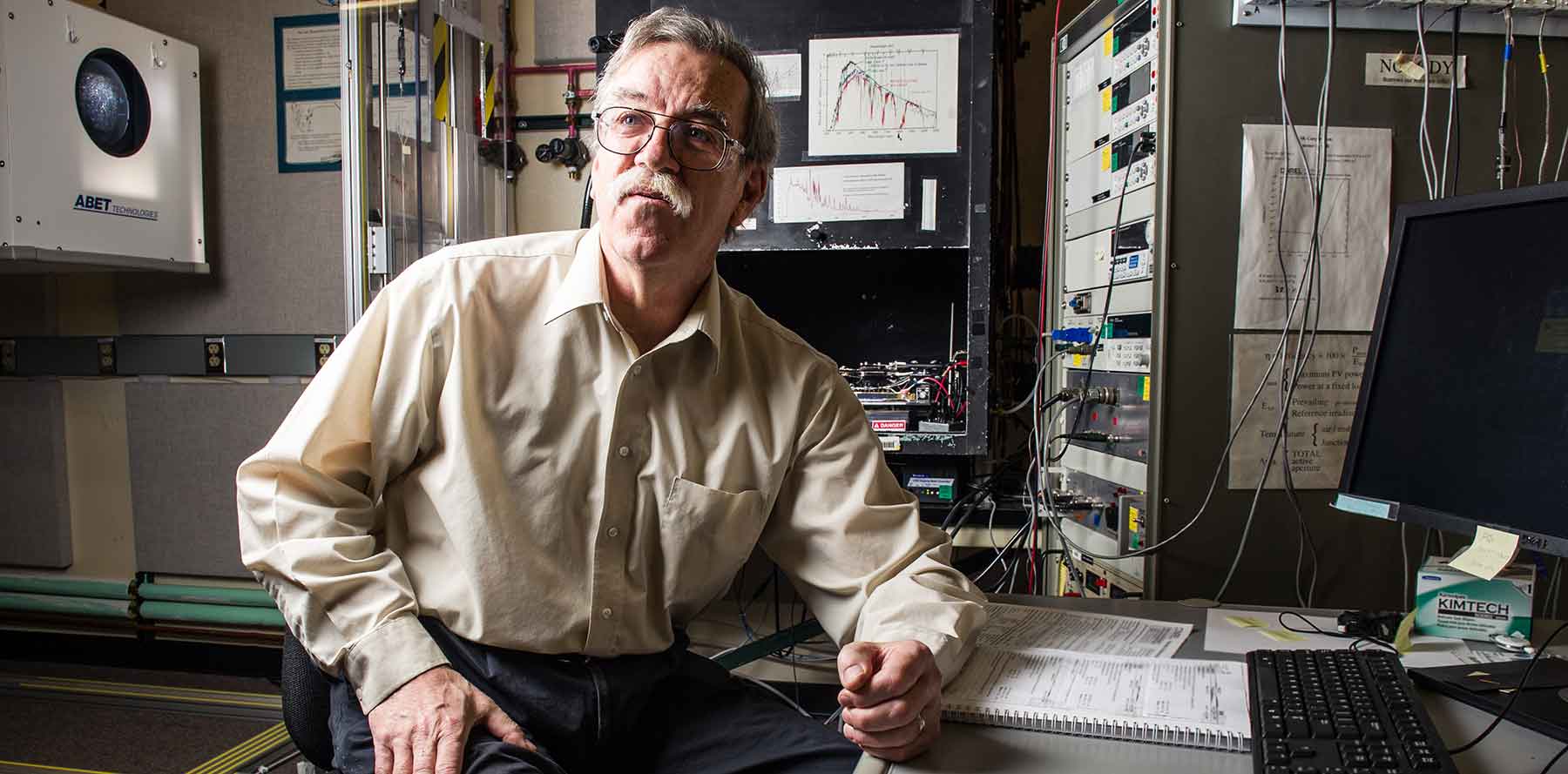 A scientist sits in a laboratory at NREL, between a solar simulator and a computer.