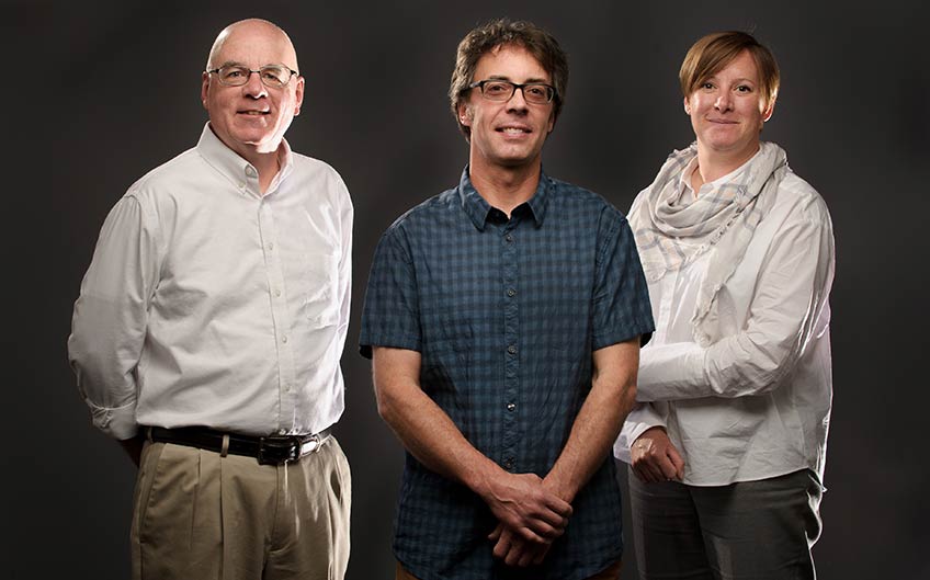 Photo shows two men and one woman standing together.