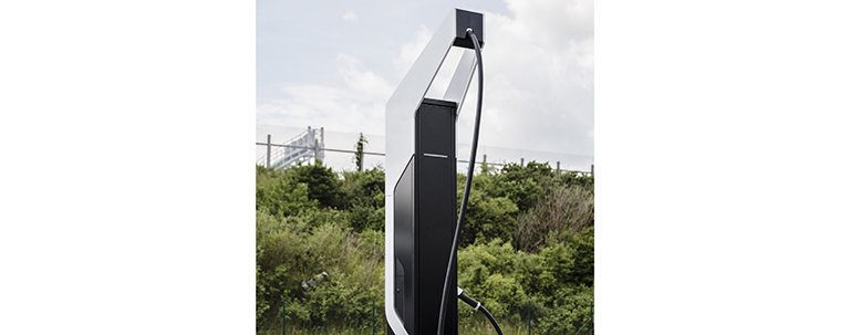 An electric vehicle charger in front of trees and shrubs.