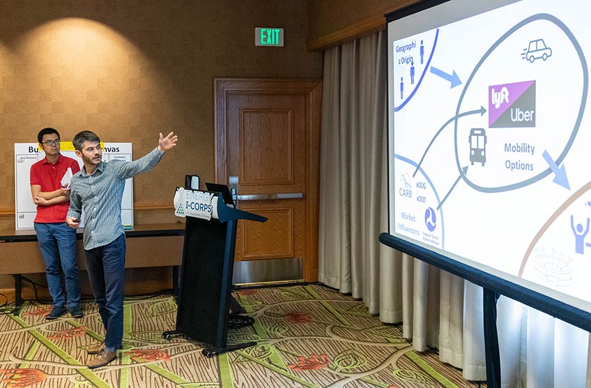 Two NREL researchers point to a screen that says "Lyft" and other icons.