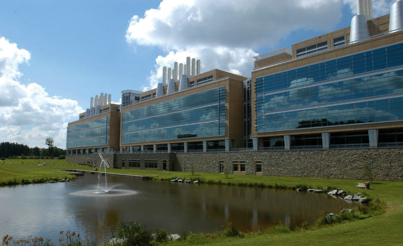 Photo of a large building with blue sky and a pond with fountain in the foreground