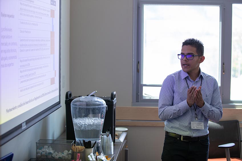 A man stands with his hands together looking a screen with a presentation.