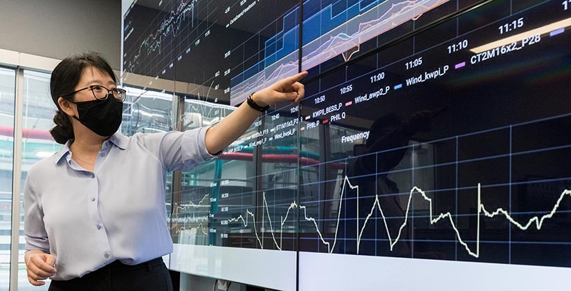 Photo of NREL power systems researcher Jin Tan examining data on a large monitor in NREL’s Energy Systems Integration Facility.