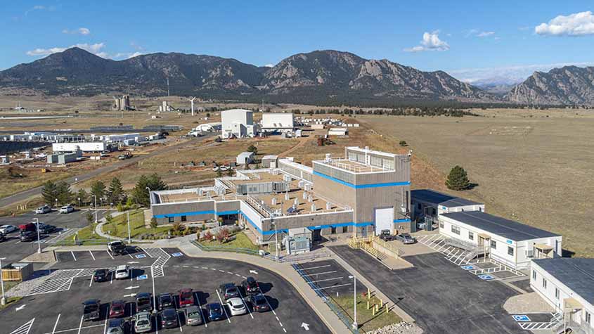 An aerial view of buildings, parking lots, and wind turbines in front of mountains