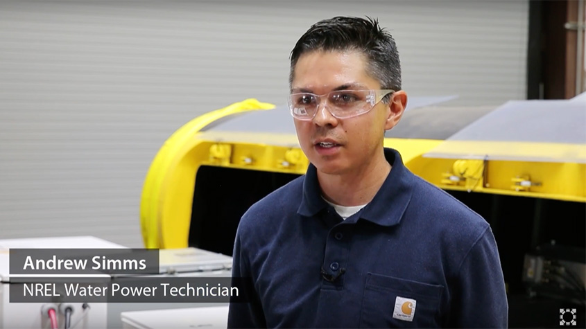 Andrew Simms wearing goggles and sitting in front of a large mechanical device with wires inside