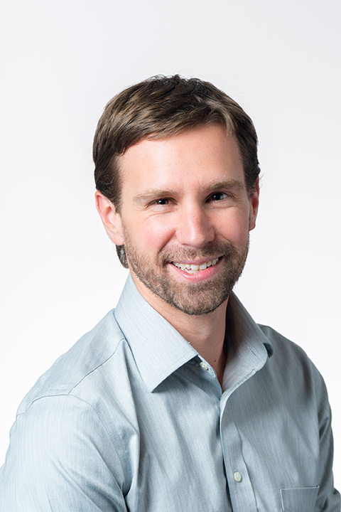 A brunette man in a light-colored button-down shirt smiles at the camera.
