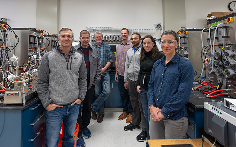 Seven researchers in safety goggles pose in a lab.