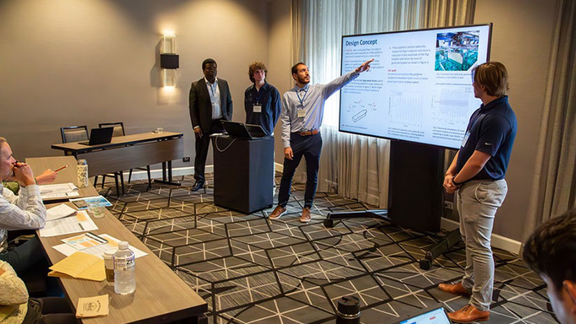 Students points to screen while other students stand at podium and present at conference