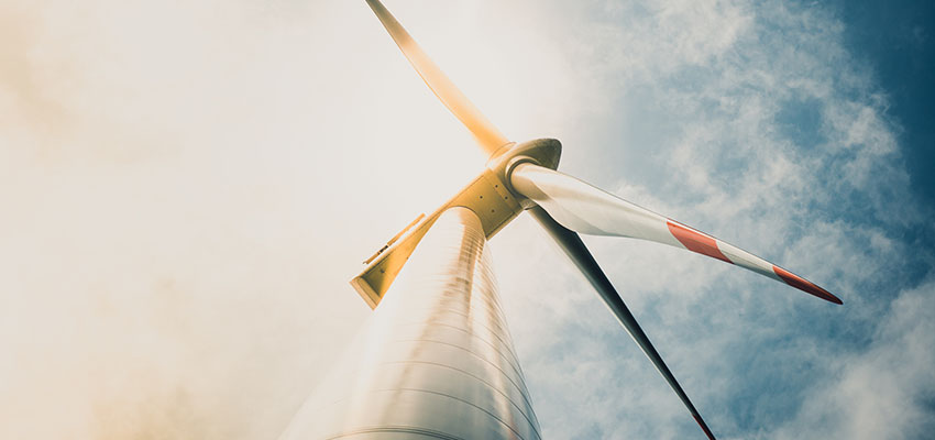 Photo of a wind turbine looking up the base of the turbine to the blades with hot smoky sky in the background.
