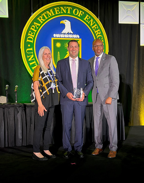Three people holding an award stand on a stage.