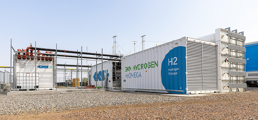 The GKN Hydrogen metal hydride system, which resembles a shipping container, sits on concrete and gravel. It is integrated with other metal structures via intricate pipe networks.
