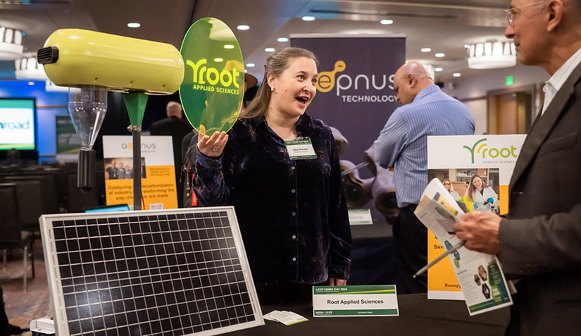 A woman standing at a table and holding a green transparent sign while talking with a man.