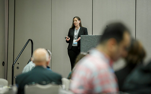 A woman standing next to a podium on stage speaking to an audience.