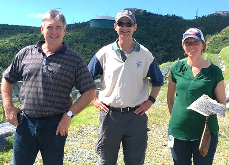 Photo of two men and a woman standing next to debris from a hurricane.