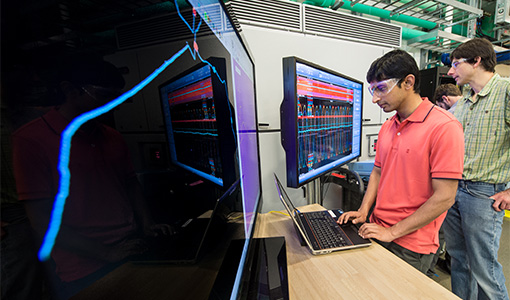 Two researchers looking at large computer monitors displaying charts and data.