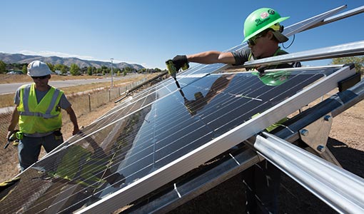 Person driving tractor in between ground-mounted solar arrays.