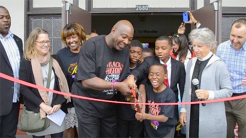 a group of happy people hold a pair of large scissors for a ribbon-cutting ceremony