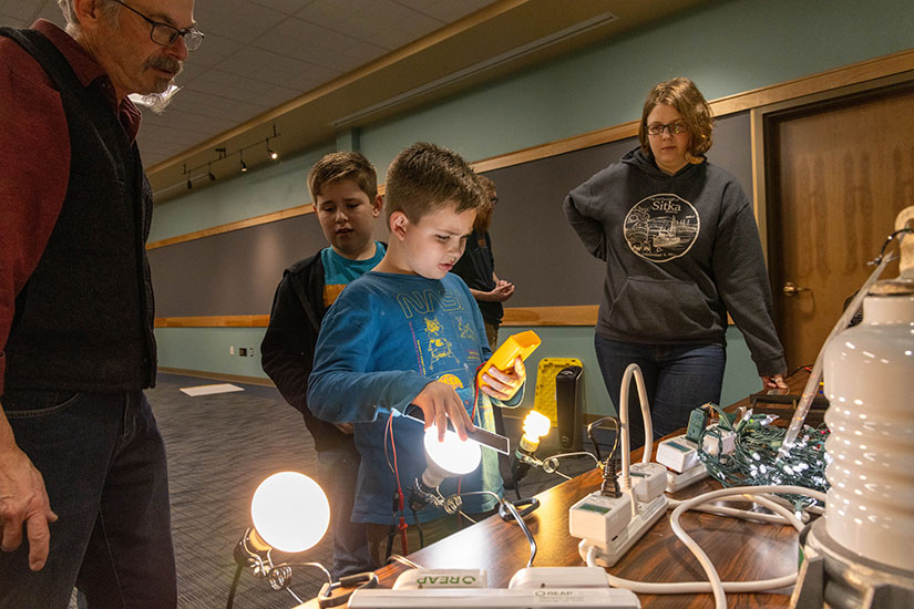 Kids learn how lightbulbs work while adults stand behind them