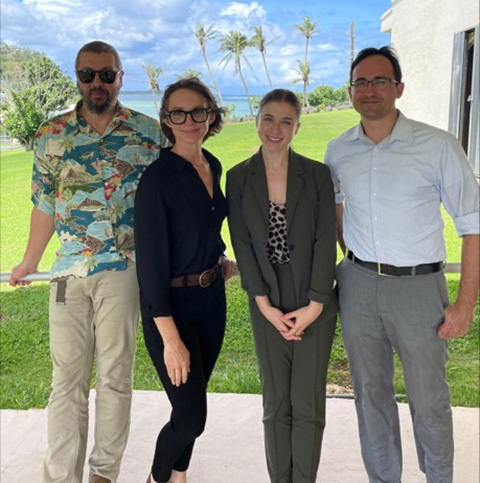 Four people under an awning smile in front of green grass and a blue sky.
