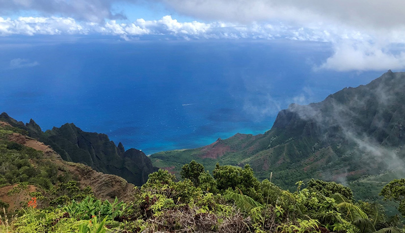 A green hilly landscape overlooking the ocean and clouds in the sky.