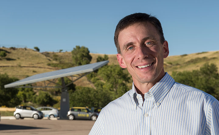 A researcher stands in font of plug-in electric vehicles charging at the rapid charging system powered by a solar canopy at the Vehicle Testing and Integration Facility at NREL.