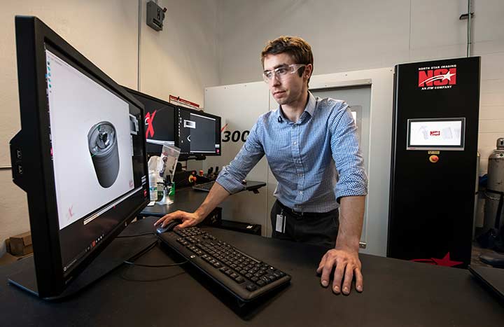 A researcher views a large computer monitor displaying a 3D image of a cylinder-shaped battery electrode