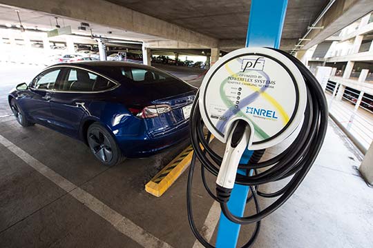 Photo of a car parked near an electric vehicle charging nozzle in a parking garage.