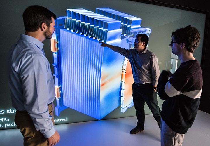 Three researchers looking at a 3-D model of a lithium-ion battery and the battery's response to mechanical-electrical-thermal failure.